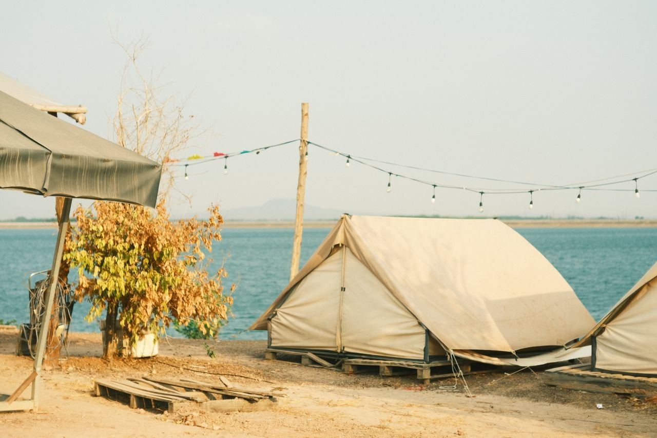 Serene camping setup by the river with tents under string lights.