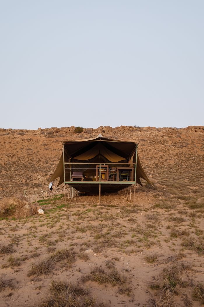 Tent with furniture on rough terrain with growing grass under gray sky in daylight